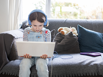 Kind mit Kopfhörer und Laptop auf einem Sofa sitzend