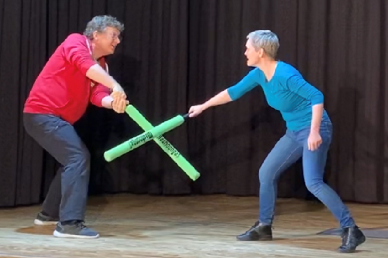 Zwei Personen kämpfen mit Schaumstoff-Schlagstöcken auf einer Bühne